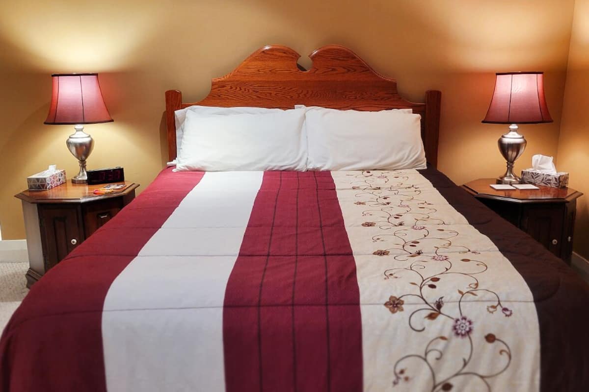 A neatly made bed with a red and white striped bedspread, two bedside tables with lamps, and a wooden headboard.