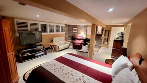 A hotel room with a large bed, a TV, a sofa, and a fireplace. - Forest Hill Bed & Breakfast (Kitchener)
