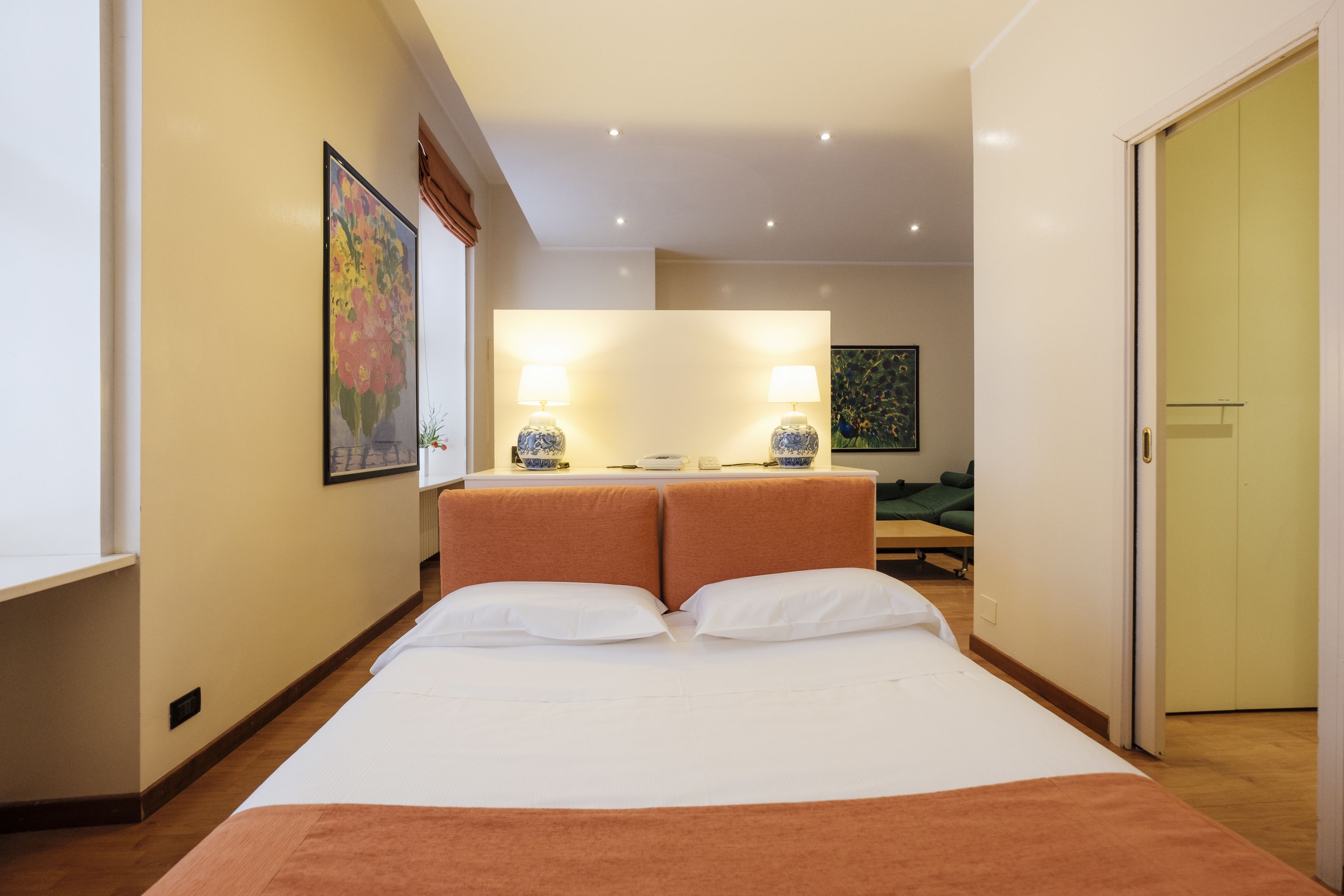 A hotel room with a large bed, two bedside lamps, a painting on the wall, and a door to the right.