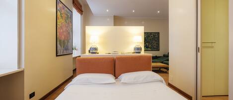 A hotel room with a large bed, two bedside lamps, a painting on the wall, and a door to the right.