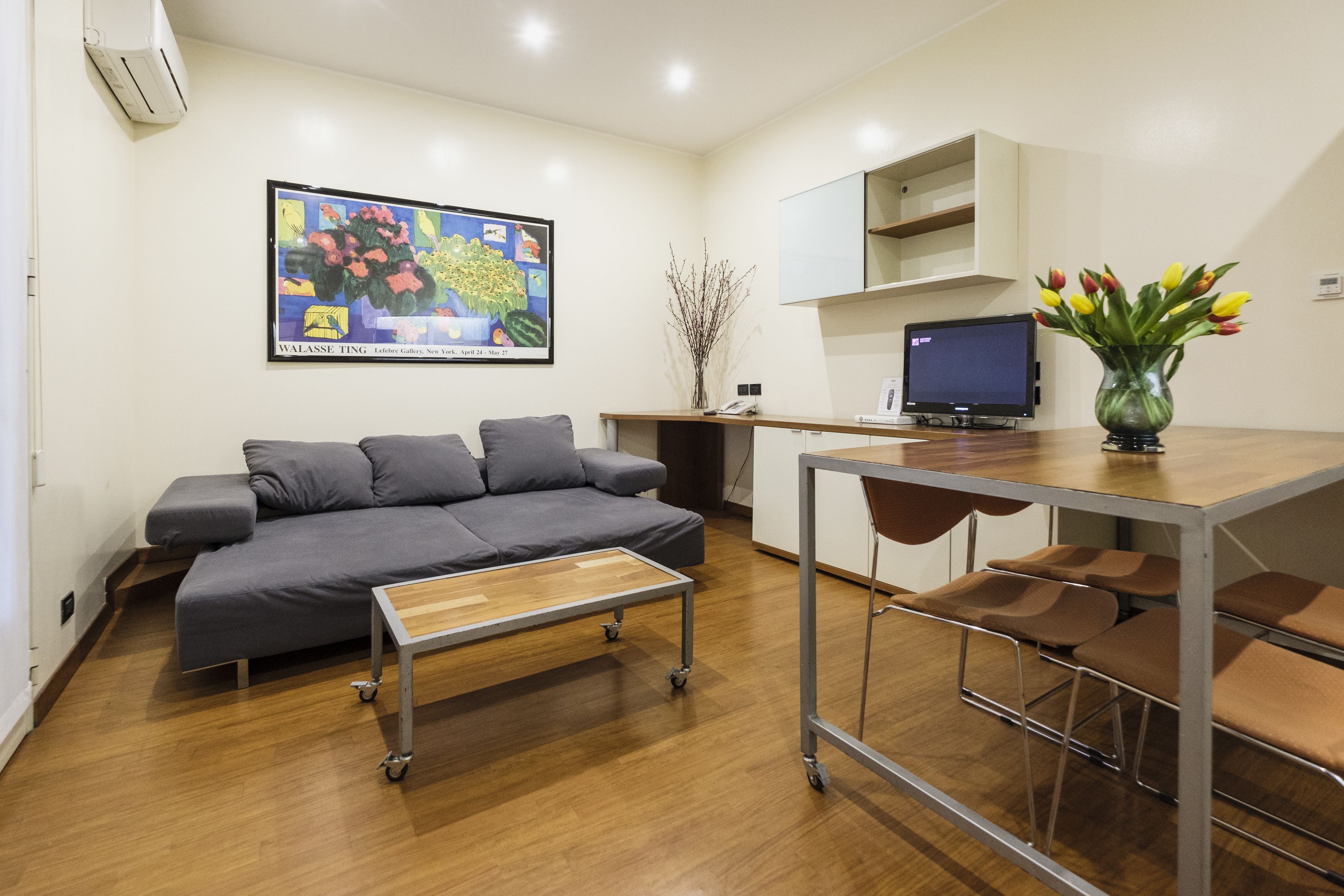 A modern living room with a grey sofa, a wooden coffee table, a TV, and a vase with flowers.