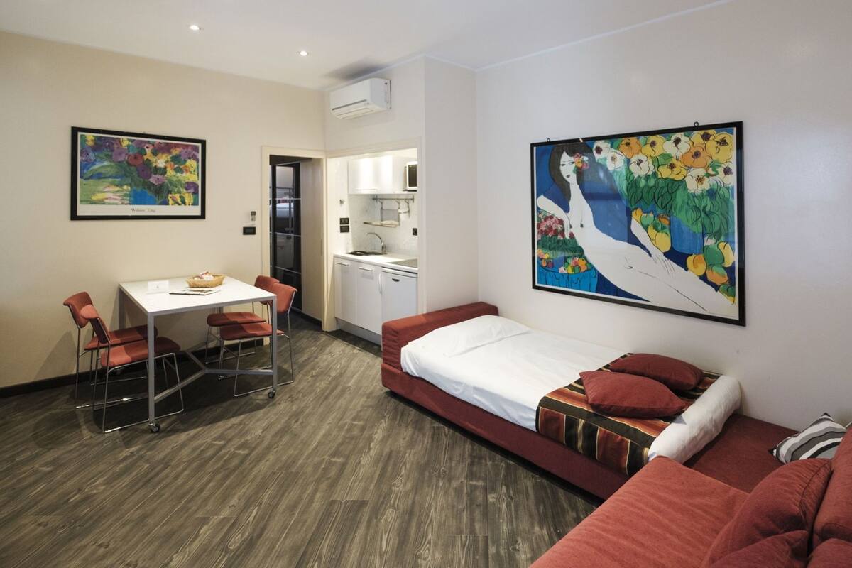 Una camera d'albergo compatta con un letto, angolo cottura, zona pranzo e due opere d'arte alle pareti.