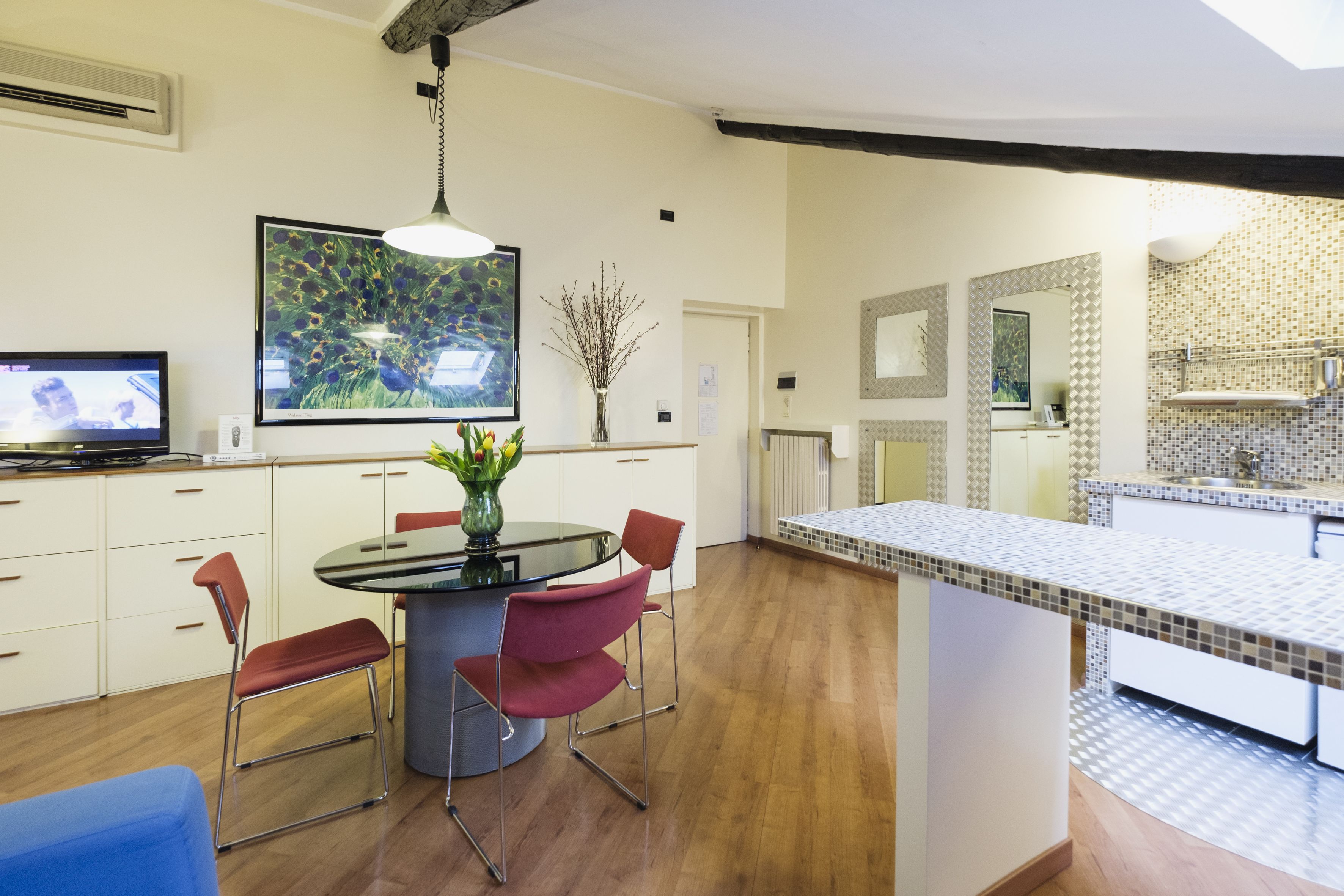 Eine moderne Küche mit Essbereich, ausgestattet mit einem runden Tisch, roten Stühlen, einer Blumenvase und einem großen gerahmten Bild an der Wand.
