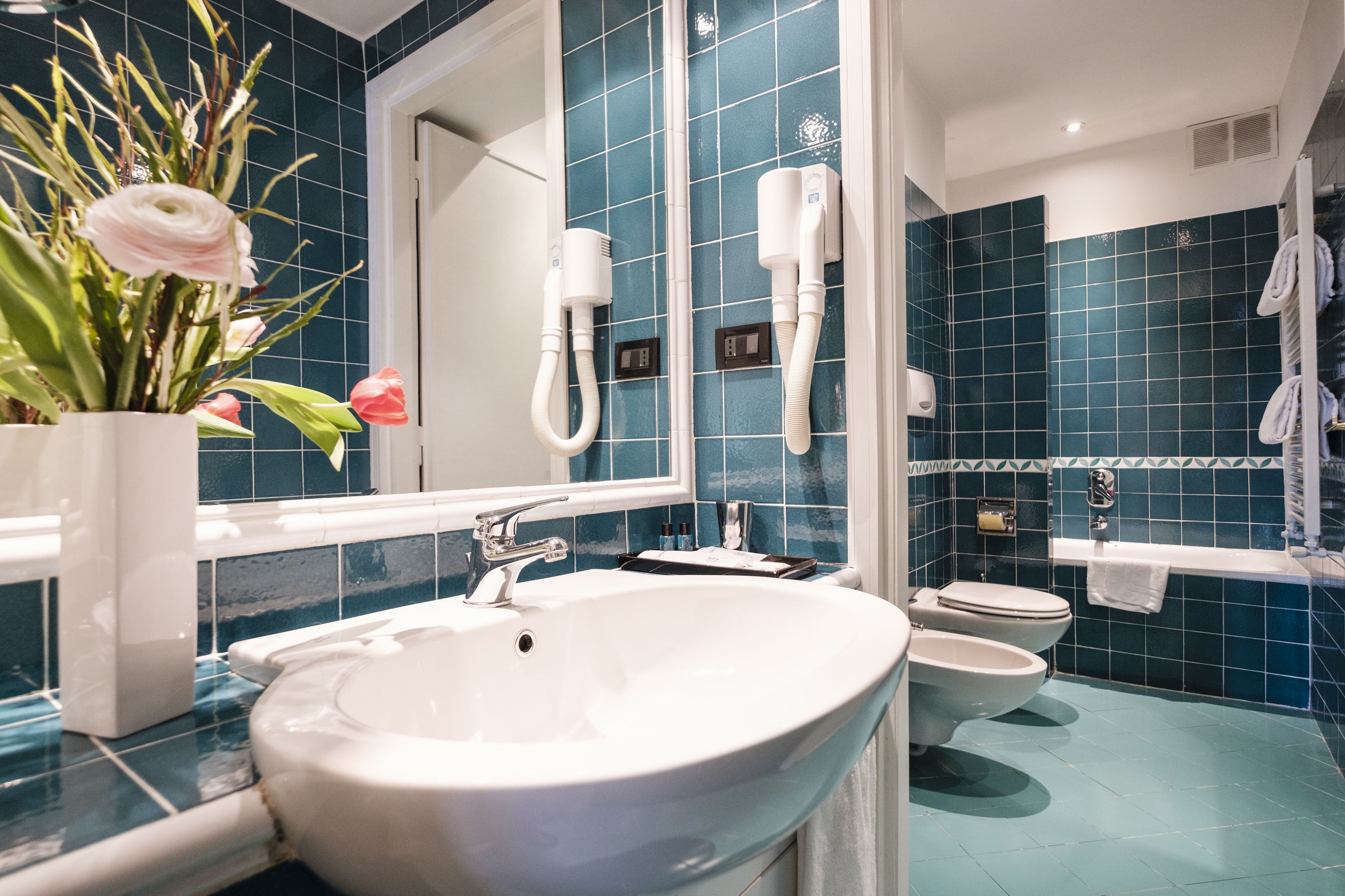 A bathroom with a white sink, a mirror, a white toilet, and a blue tiled wall.