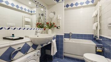 Ein Badezimmer mit einem weißen Waschbecken, einer Badewanne und einer Toilette. Über dem Waschbecken befindet sich ein Spiegel und an der Wand ein Handtuchhalter.
