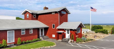 Un edificio rojo con una bandera, un estacionamiento y vista al mar.