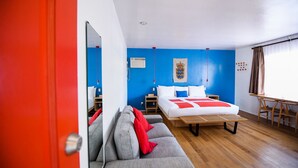 A modern hotel room with a large bed, a sofa, a desk, and a window with curtains.