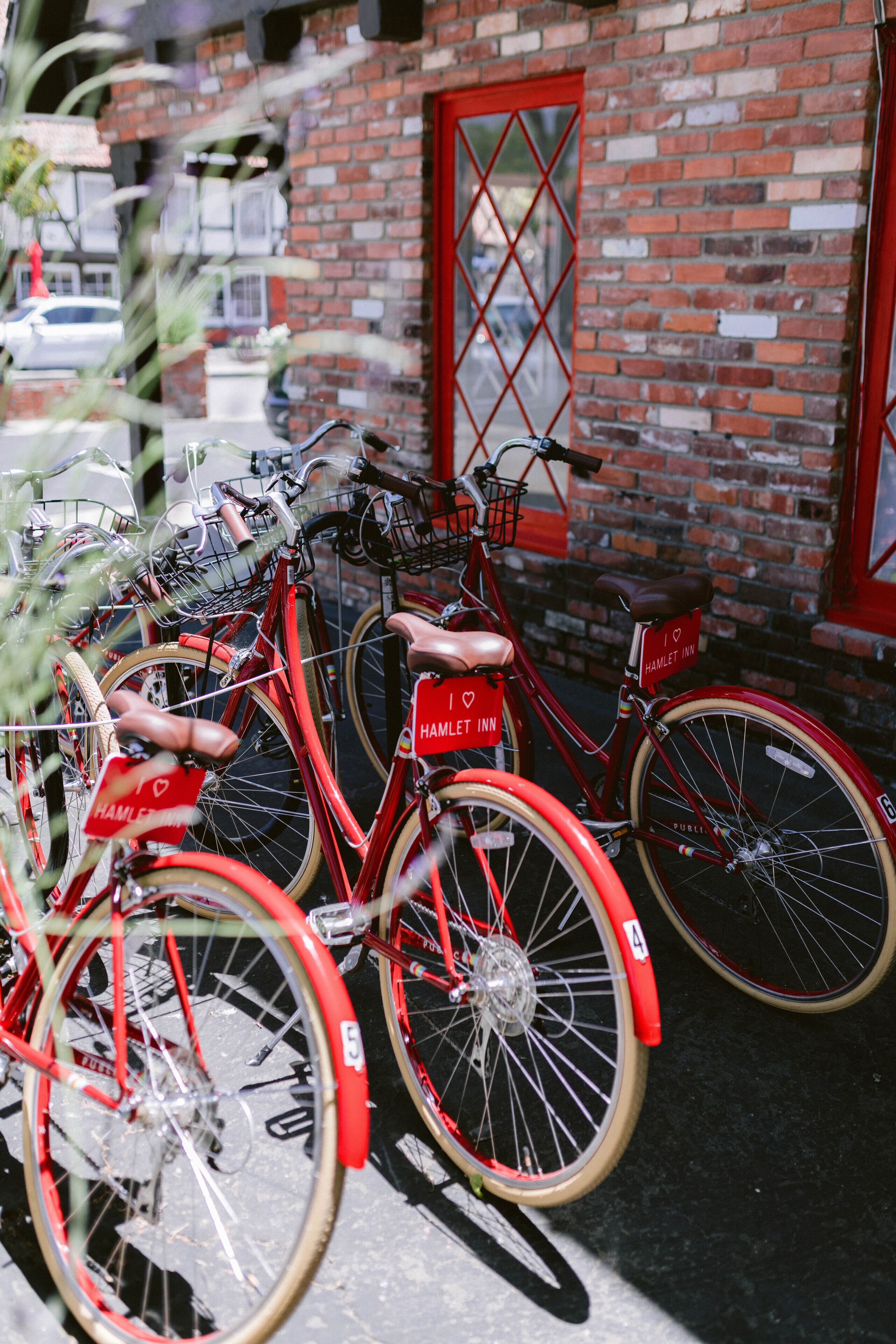 A red bicycle with a "I ♥ HAMLET INN" sign, parked in front of a brick building with a red door.
