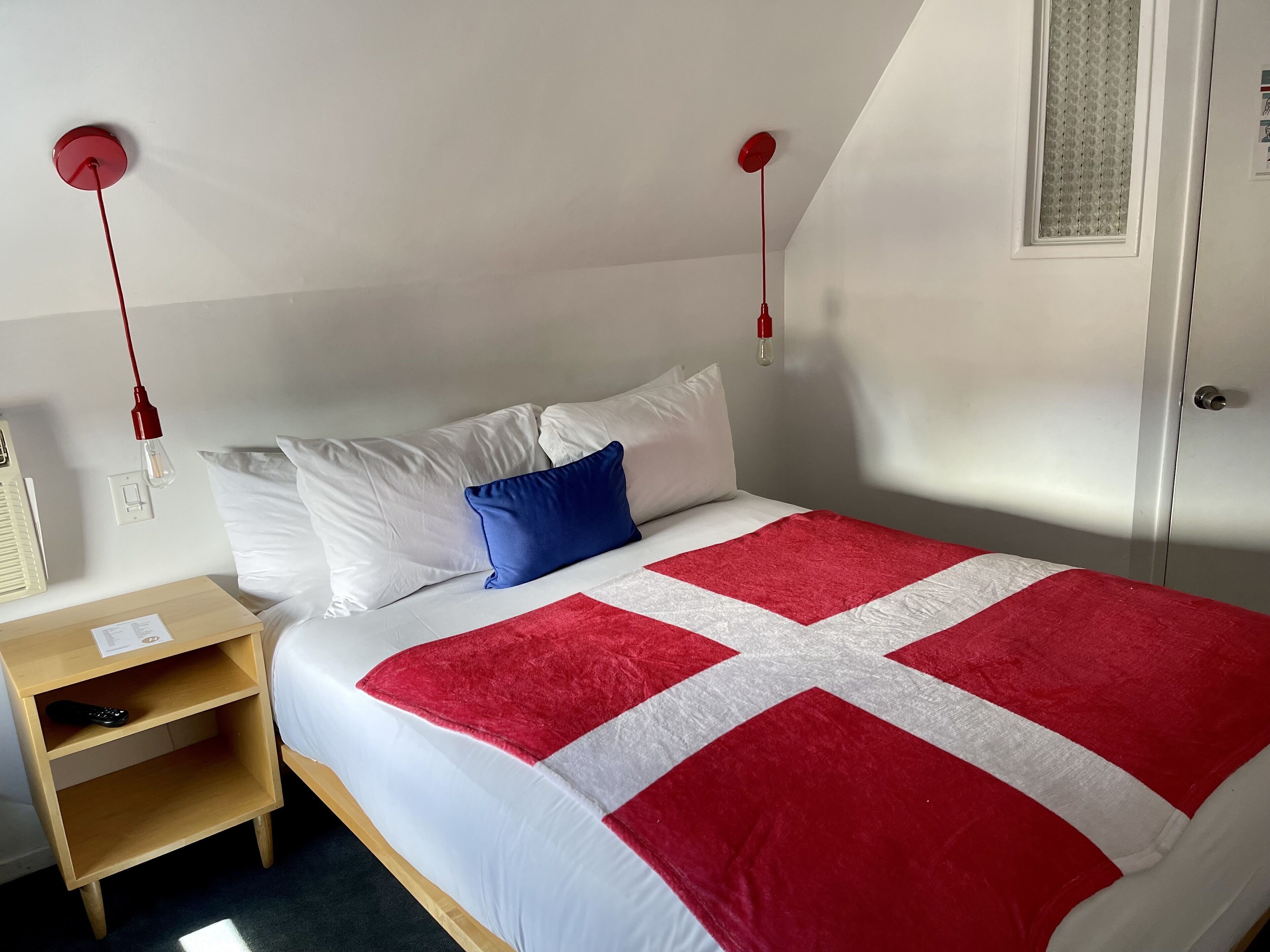 A bedroom with a bed, pillows, a nightstand, and a red and white quilt.