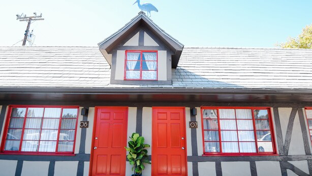 A building with two red doors, a small balcony with a bird sculpture, and a potted plant in front.