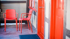 Two red chairs outside a building with a red door and windows.
