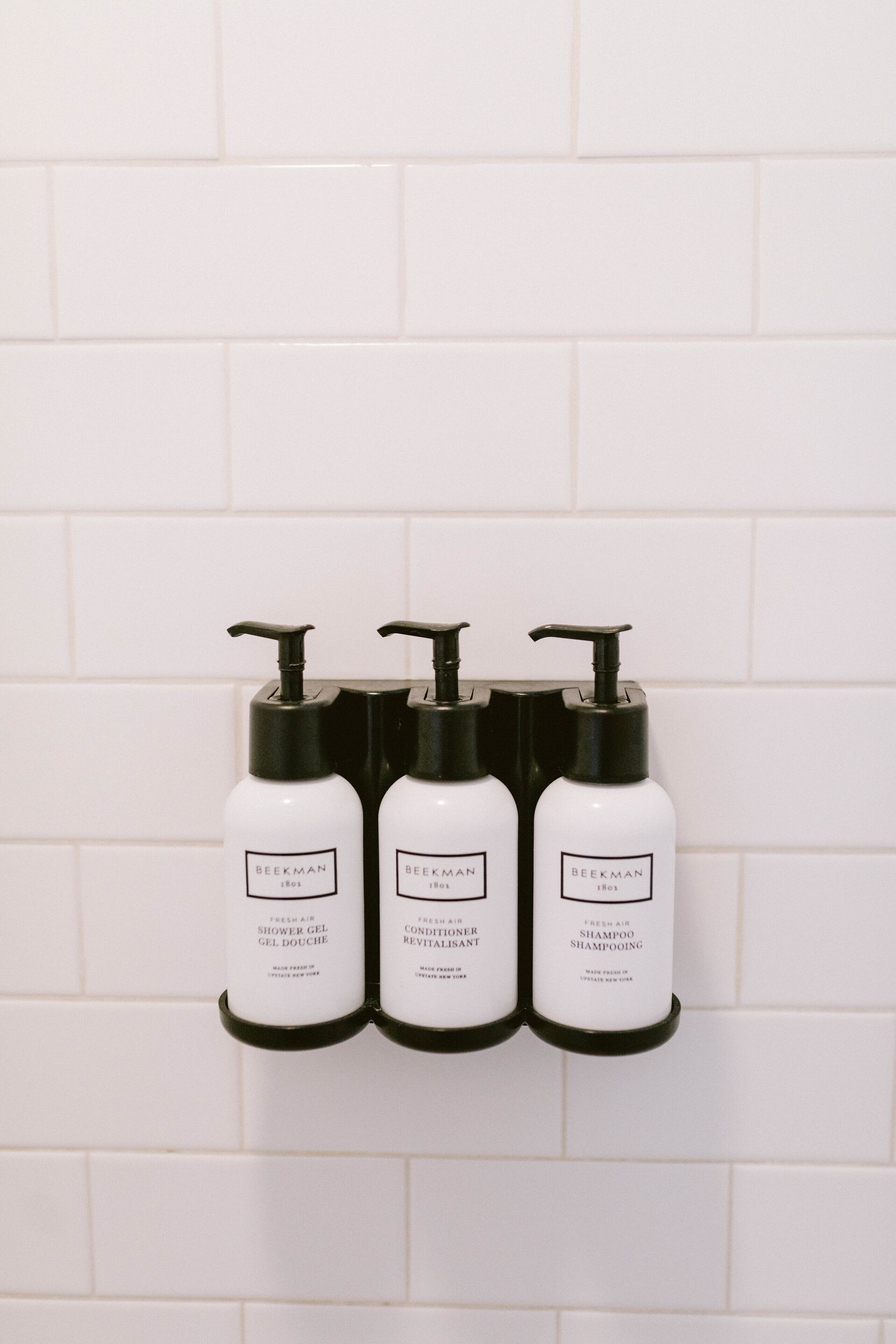 Three white bottles with black pumps on a white tiled wall.