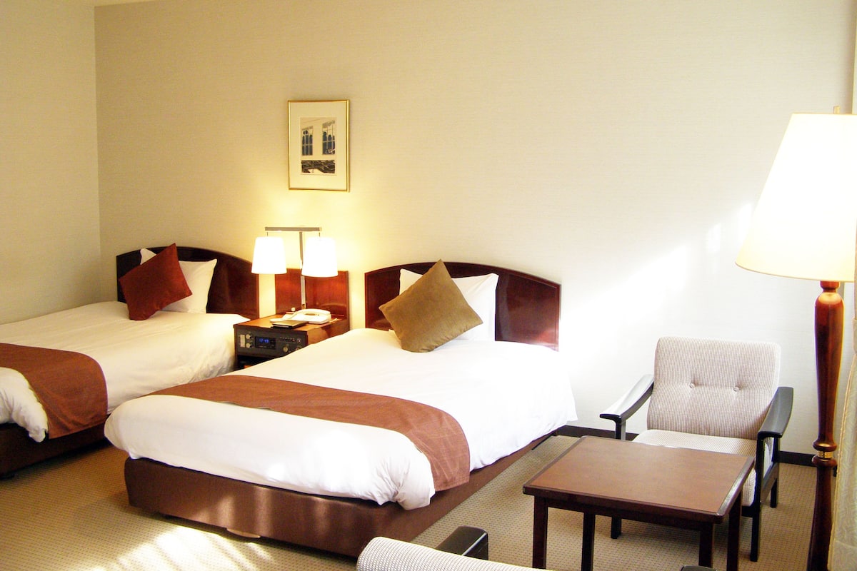 Une chambre d’hôtel avec deux lits, une table de chevet avec des lampes, une chaise et une table.
