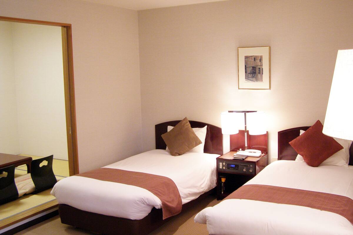 Une chambre d’hôtel avec deux lits, une table de chevet avec une lampe, une horloge et un tableau encadré au mur.