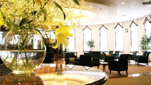 A spacious lobby with a large vase of yellow lilies and baby's breath on a reflective surface. There are multiple seating areas with chairs and tables. - Hotel Marroad Karuizawa (Karuizawa)