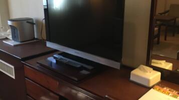 A hotel room with a wooden desk, a flat-screen TV, a coffee maker, and a tissue box.