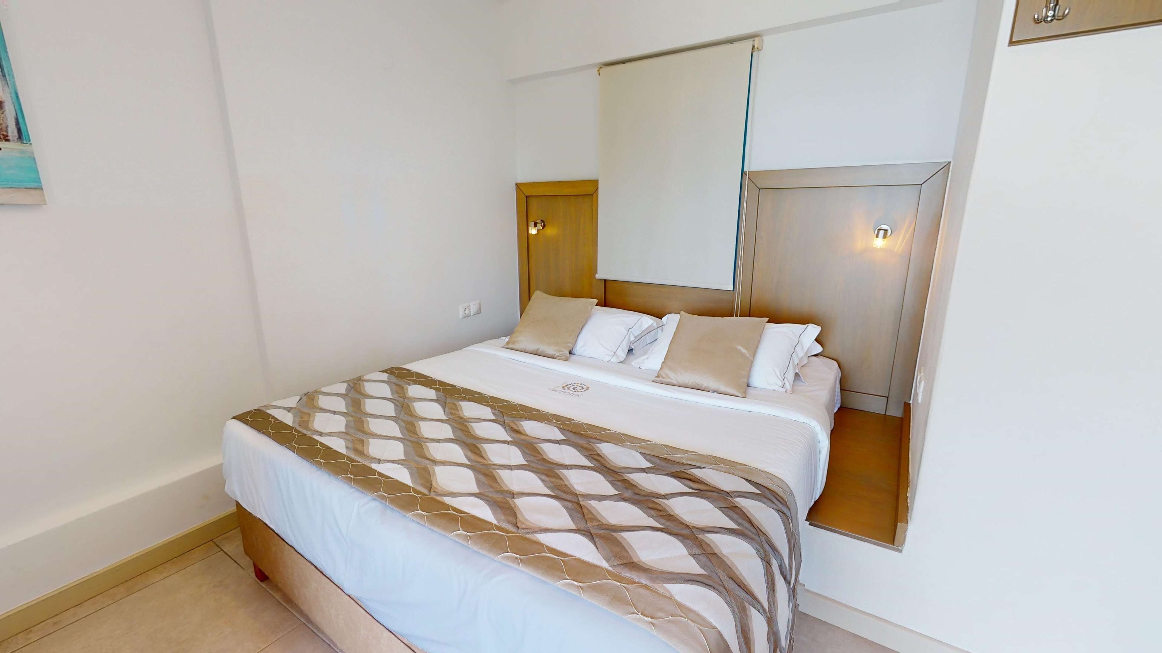 A bedroom with a bed, a headboard, a wall-mounted mirror, and a light fixture.