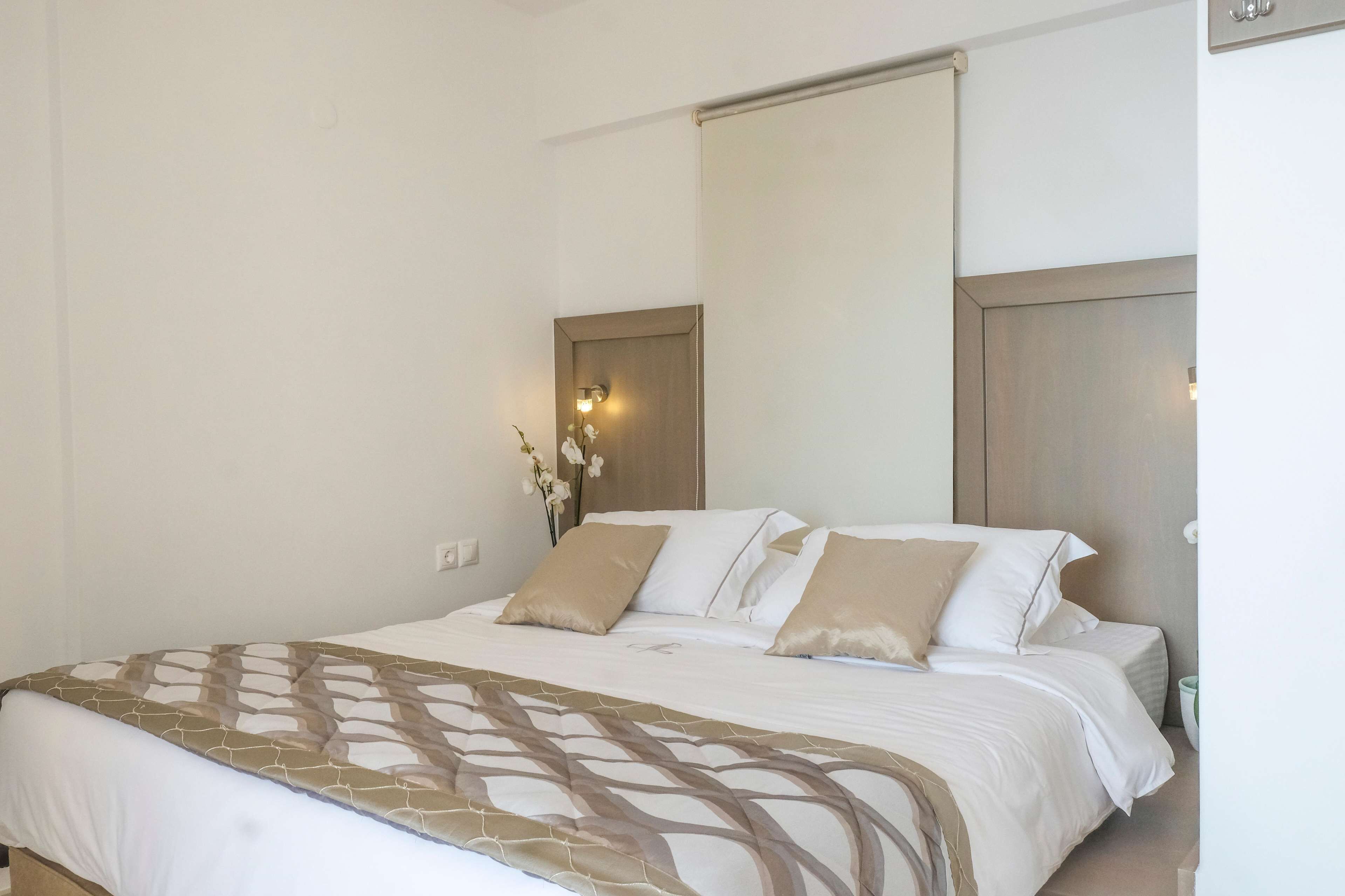 A neatly made bed with a patterned bedspread, a wall-mounted light fixture, and a small vase with flowers.