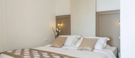 A neatly made bed with a patterned bedspread, a wall-mounted light fixture, and a small vase with flowers.