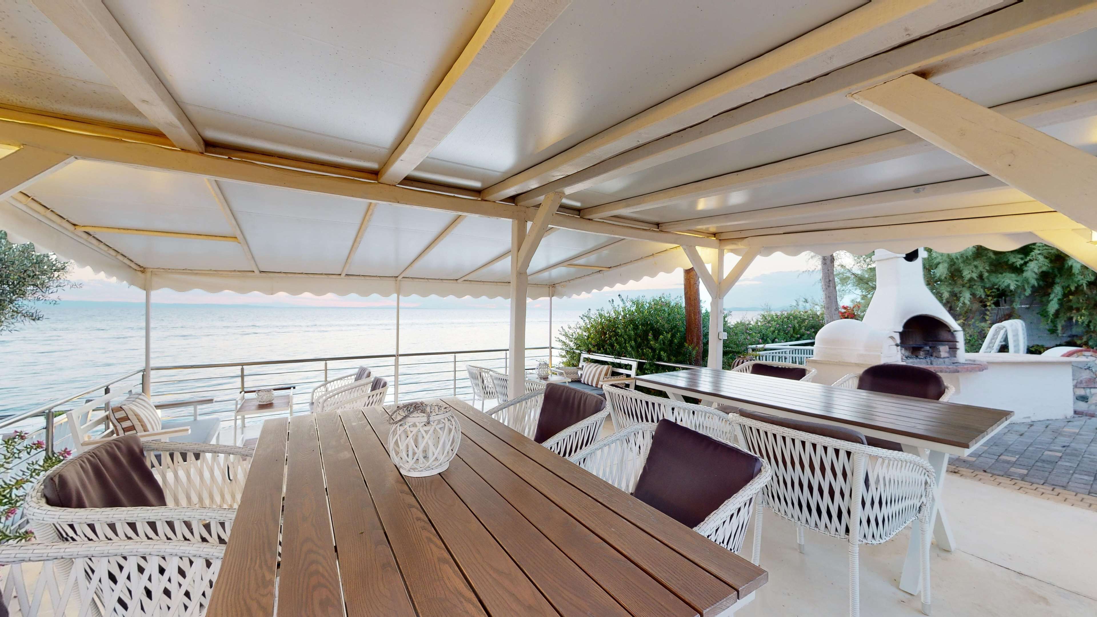 A covered outdoor seating area with wicker furniture, a wooden table, and a stone oven.