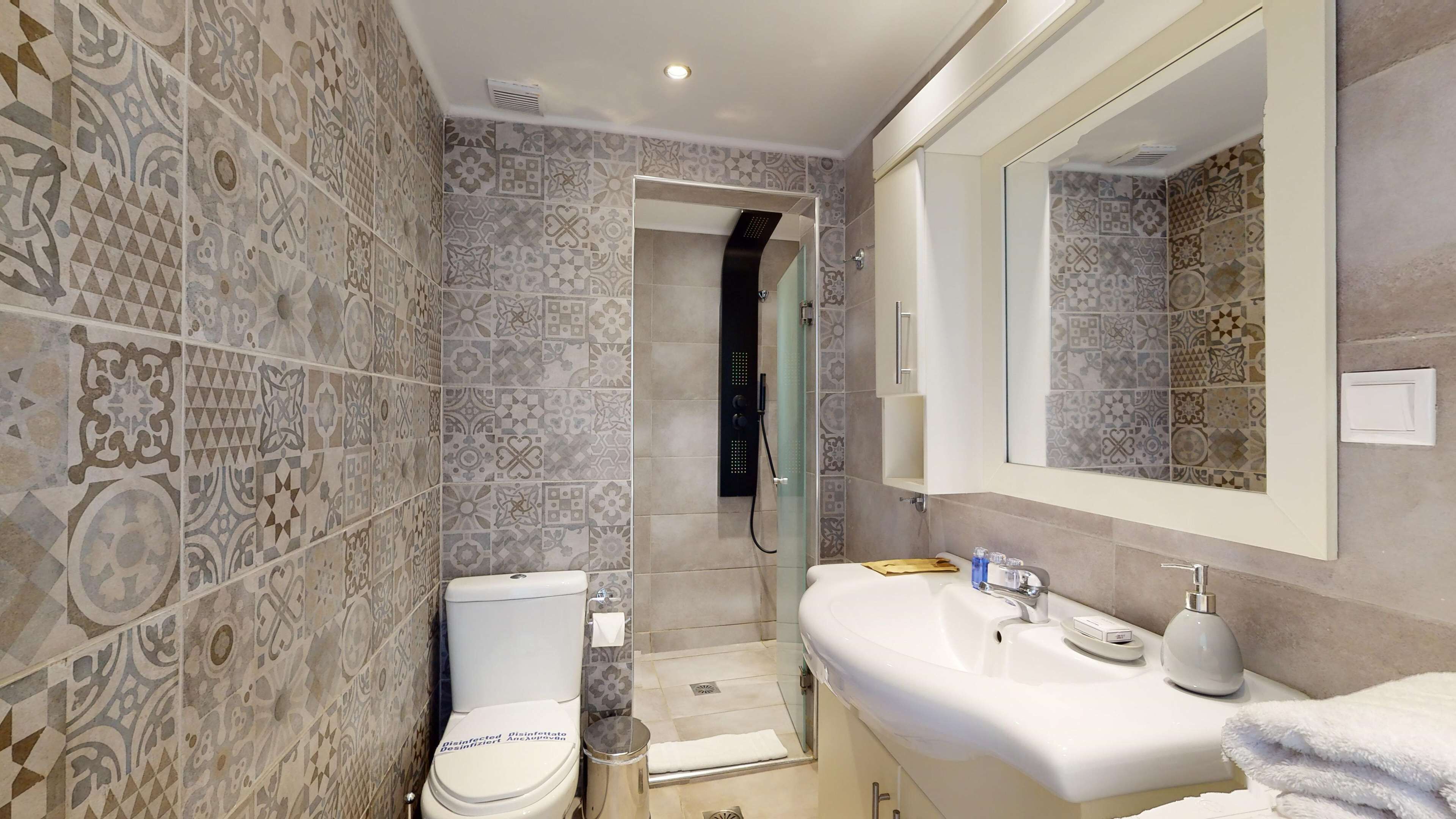 Une salle de bain avec des carreaux décorés, des toilettes, une douche et un lavabo avec un miroir.