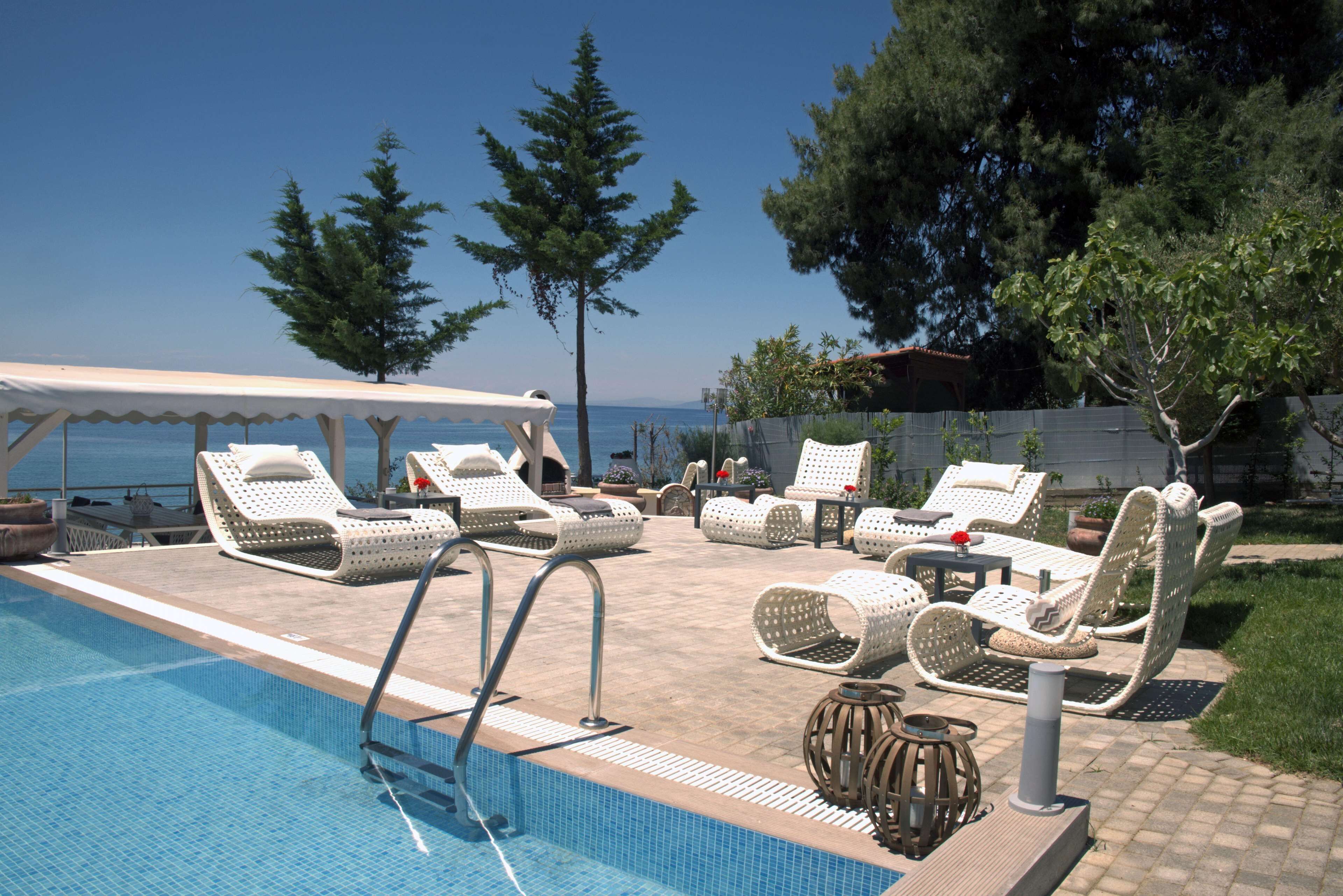 A poolside area with lounge chairs and a covered seating area, overlooking a body of water.