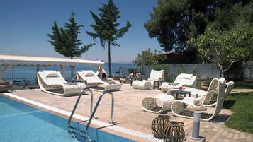 A poolside area with lounge chairs and a covered seating area, overlooking a body of water.
