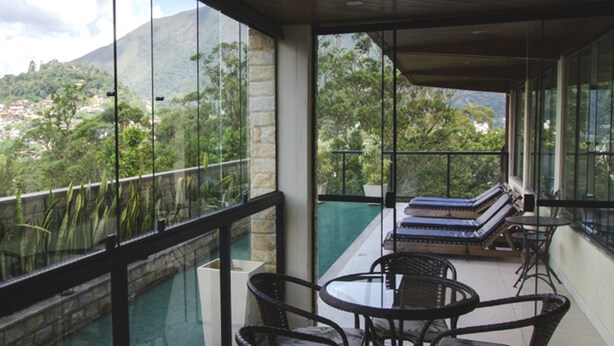 A balcony with a view of a mountainous landscape, furnished with wicker chairs and a table. - Hotel Willisau (Teresópolis)
