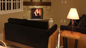 A living room with a stone fireplace, a black sofa, and a wooden coffee table. - Hotel Willisau (Teresópolis)