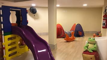 Uma área de recreação infantil com um escorrega roxo, tendas de brincar e um brinquedo de sapo.
