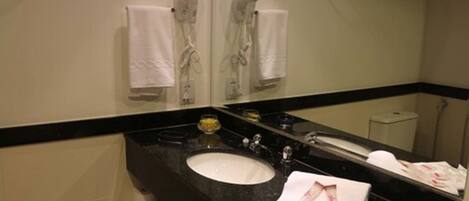 A bathroom with a black countertop, a white sink, and a mirror reflecting a towel and a hairdryer.