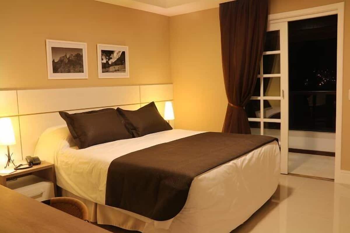 Une chambre d’hôtel avec un lit, une table de chevet, une lampe et deux tableaux encadrés accrochés au mur.