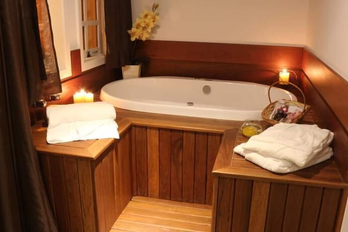 Une baignoire en bois, avec un banc en bois de chaque côté, une bougie et un panier rempli de produits de toilette.