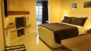 A bedroom with a stone fireplace, a bed with dark bedding, and two framed pictures on the wall. - Hotel Willisau (Teresópolis)