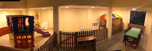 Zona de juegos infantiles con un tobogán, estructuras de juego y un área con mesa amurallada.