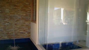 Um banheiro com chuveiro em box de vidro, parede de tijolos e piso azul.