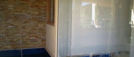 A bathroom with a glass-enclosed shower, a brick wall, and a blue-tiled floor.