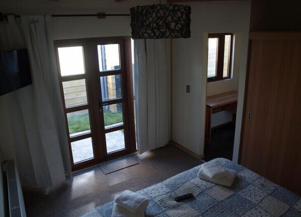 A room with a bed, a desk, and a window overlooking a garden. - Cabañas Shenu Patagonia (Punta Arenas)
