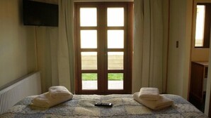 A bedroom with a large bed, two towels, a remote control, and a window with curtains.