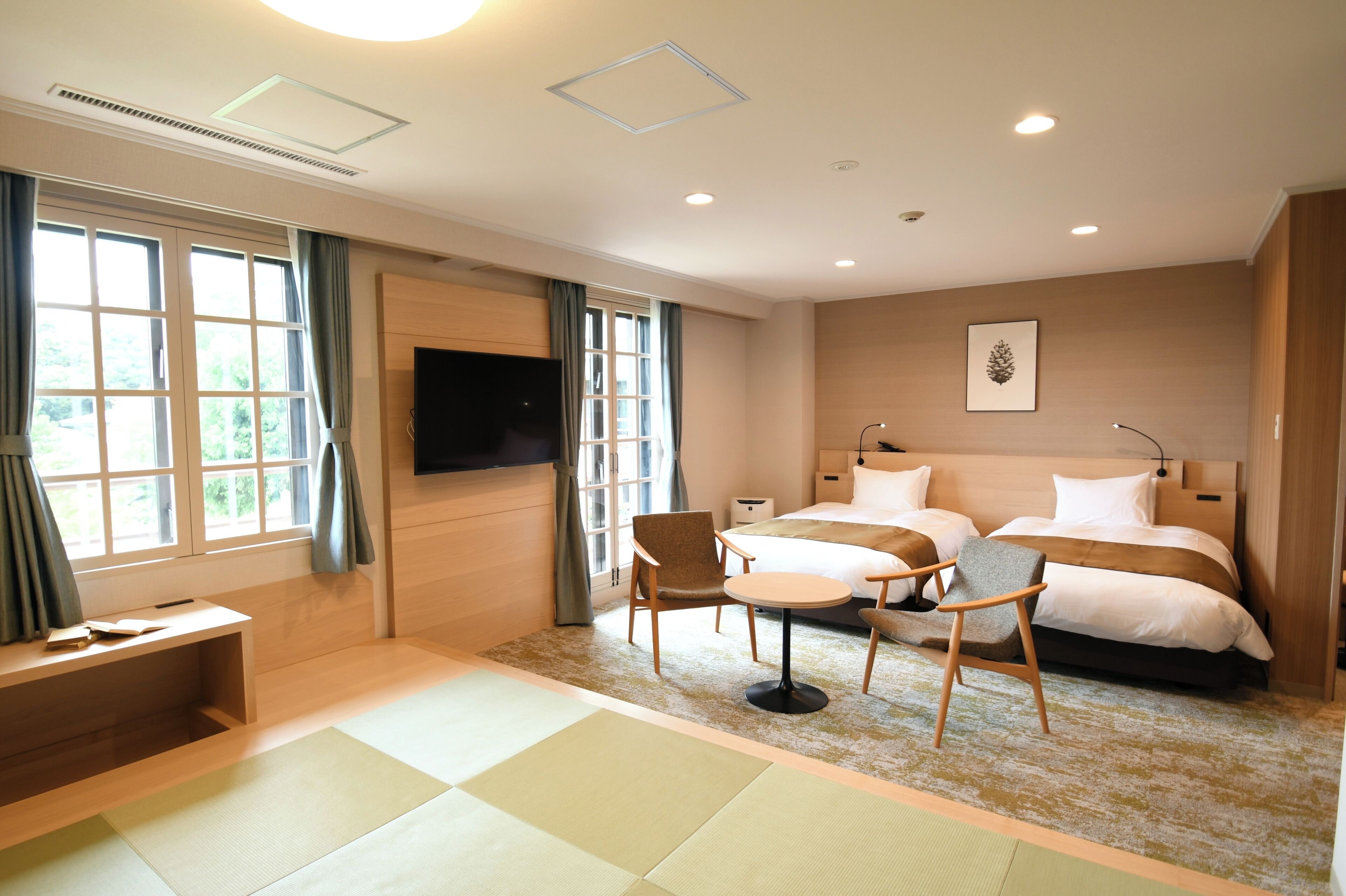 A hotel room with a bed, two chairs, a desk, a TV, and a window with curtains.