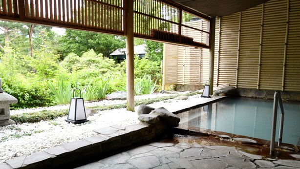 A stone-tiled pool area with a bamboo fence, surrounded by a garden with various plants and a stone lantern. - Marroad Hakone (Hakone)