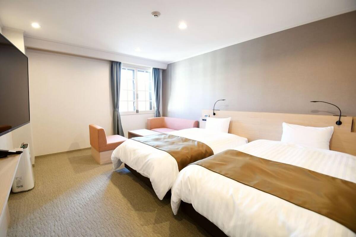 A hotel room with two beds, a TV, a desk, and a window with curtains.