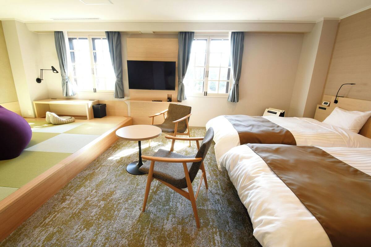 A hotel room with a bed, a sofa, a small table, a chair, a TV, and a window with curtains.