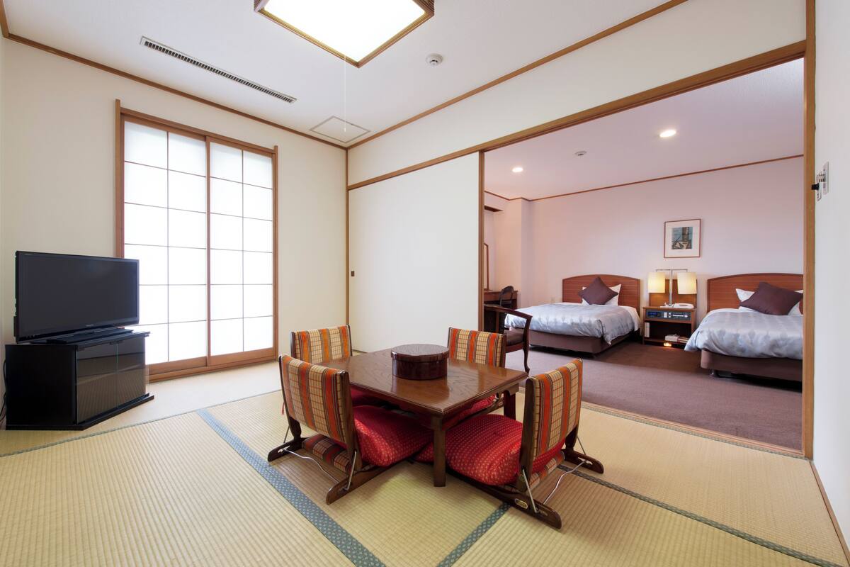 A hotel room with tatami flooring, a traditional Japanese-style dining table, and two beds.