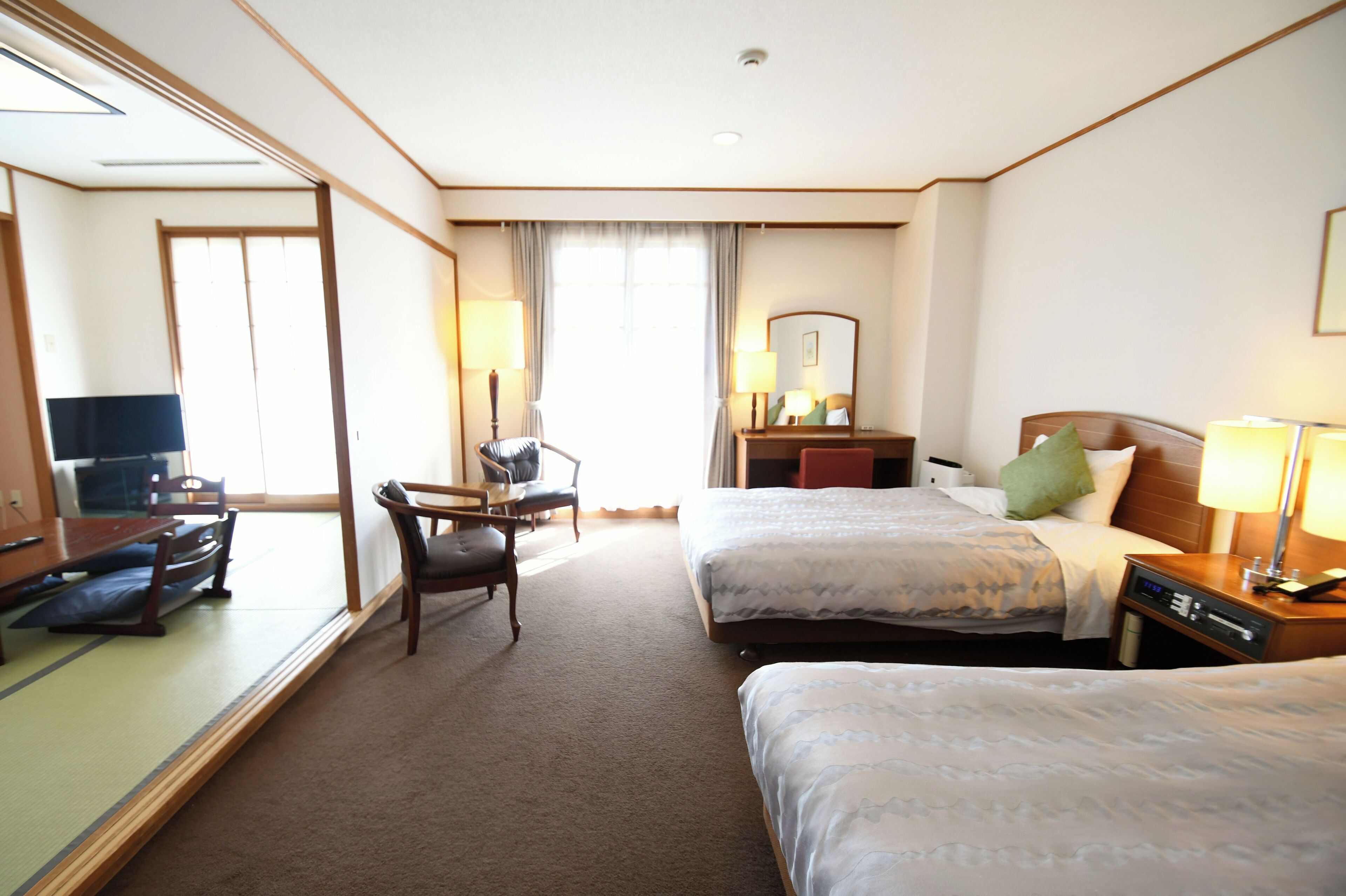 Ein Hotelzimmer mit zwei Betten, einem Schreibtisch, einem Sessel, einem Fernseher und einem großen Spiegel.
