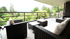 A balcony with wicker furniture, a glass table, and a view of greenery. - Marroad Hakone (Hakone)