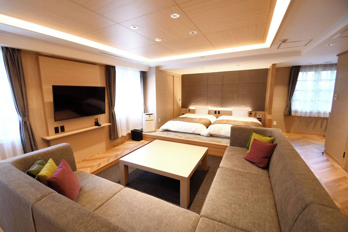 A modern hotel room with a large bed, a sofa, a TV, and a flat-screen TV mounted on the wall.