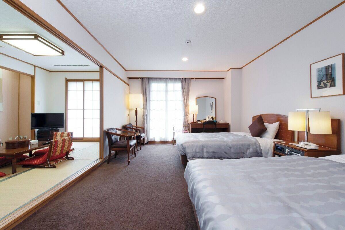 A hotel room with two beds, a desk, a chair, a television, and a large mirror.
