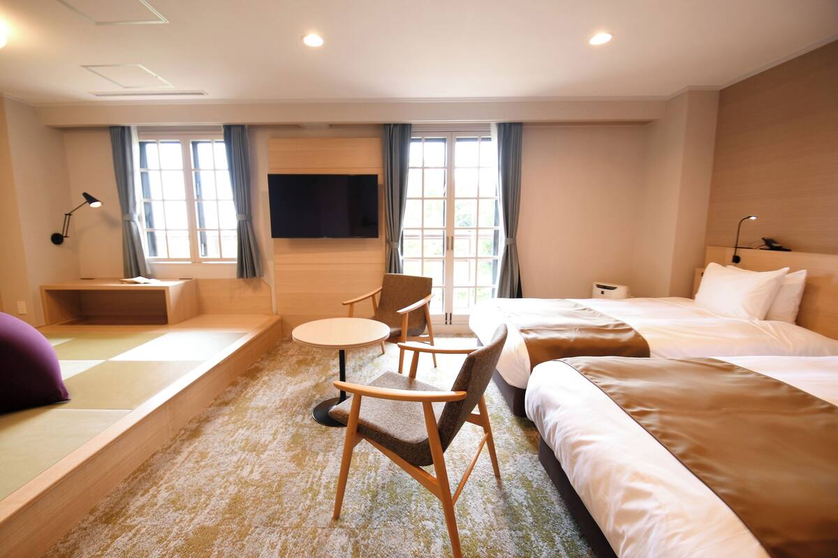 A hotel room with a bed, a desk, a chair, a TV, and a window with curtains.