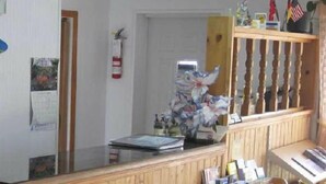 A reception area with a wooden counter, a fire extinguisher, and various wall decorations including a clock and a framed certificate. - Rosecourt Motel (Stratford)